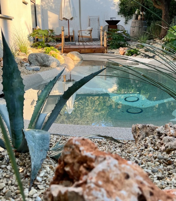 Création de piscine lagon sur mesure avec intégration paysagère Piscine lagon paysagée avec terrasse bois et aménagement minéral par CAP PAYSAGES